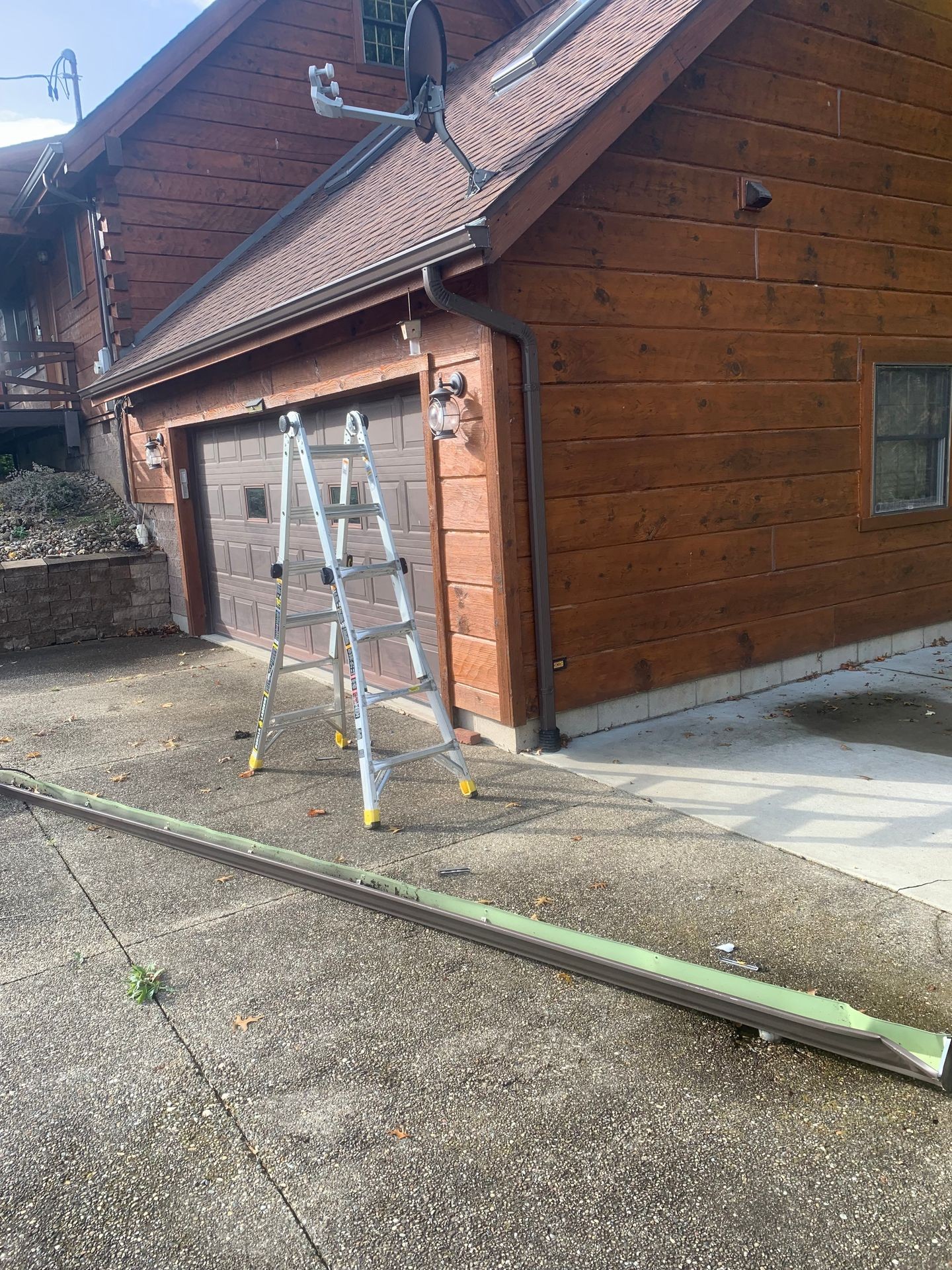 Wooden house exterior with a ladder and detached rain gutter on the driveway.